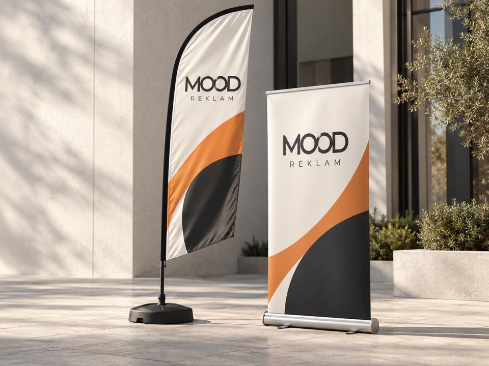 Bina girişinde yan yana duran MOOD REKLAM yelken bayrak ve roll-up banner