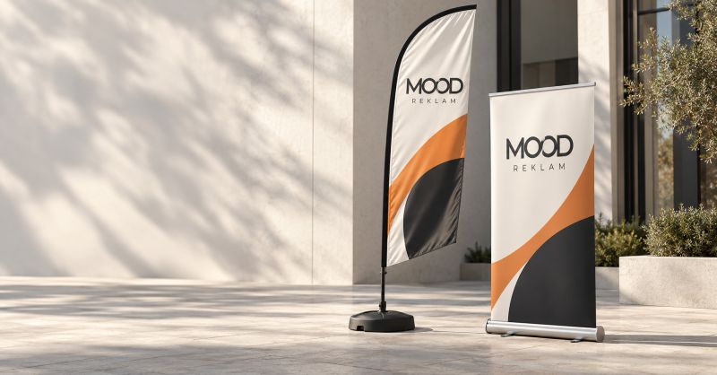 Bina girişinde yan yana duran MOOD REKLAM yelken bayrak ve roll-up banner